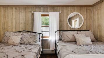 Un dormitorio con dos camas, paredes de madera, una ventana con cortinas y un espejo en la pared.