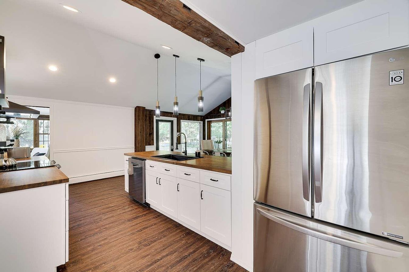 A modern kitchen with white cabinetry, a stainless steel refrigerator, and wooden flooring.