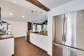 A modern kitchen with white cabinetry, a stainless steel refrigerator, and wooden flooring.