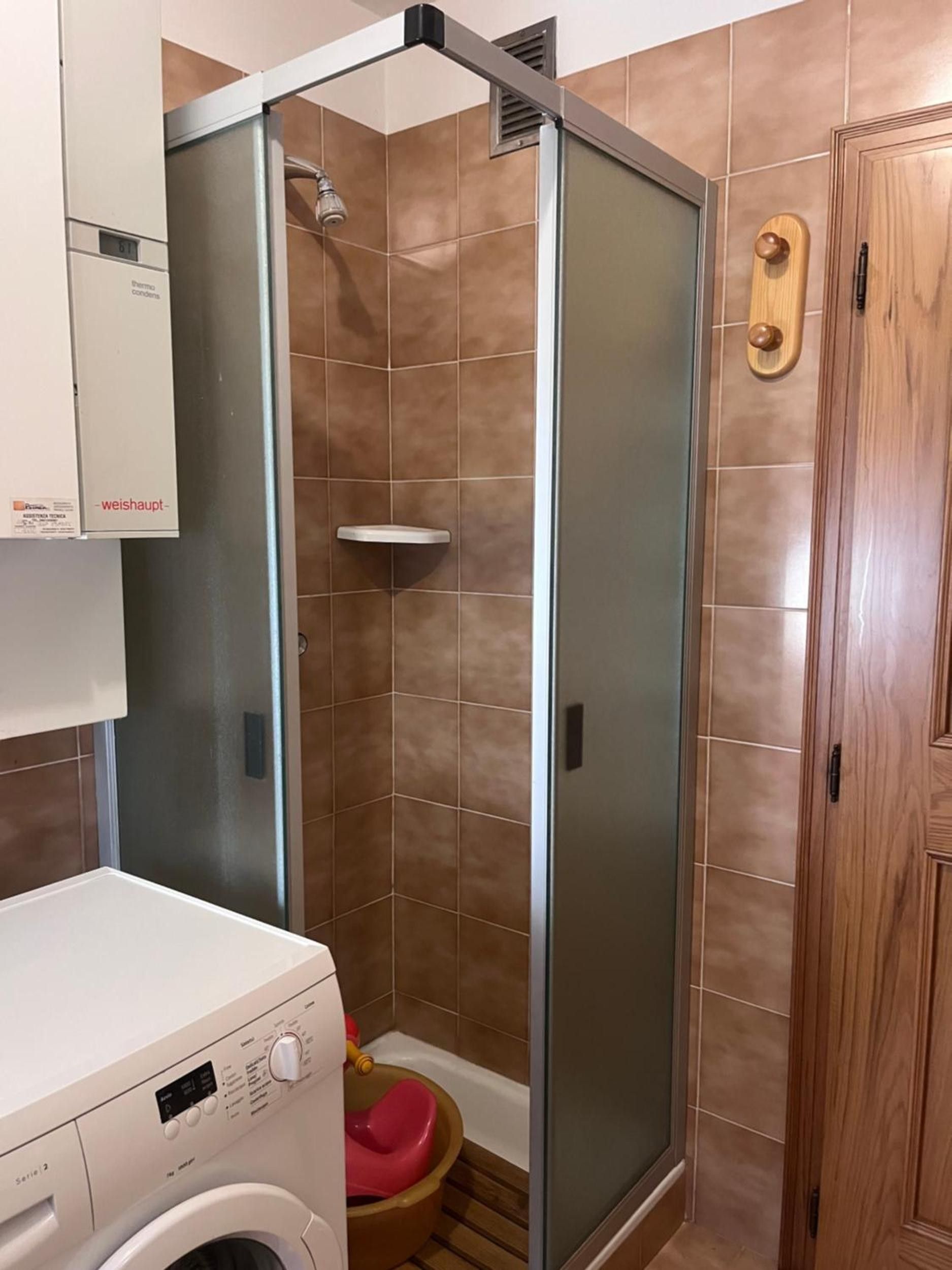 Une salle de bain avec une douche à parois de verre, un lave-linge et une porte en bois.