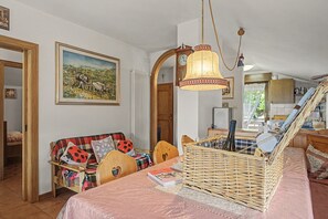 A cozy room with a wooden floor, a sofa with patterned cushions, a wicker basket, and a painting on the wall.