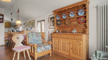 Un intérieur traditionnel avec un meuble en bois où sont exposées des assiettes en céramique, un fauteuil recouvert d’un tissu à motifs floraux et une horloge ancienne.