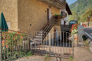 A rustic building with a stone facade, a wooden staircase, and a metal gate.