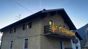 Ein zweistöckiges Gebäude mit Balkon, einer sichtbaren Antenne und einem Berg im Hintergrund.