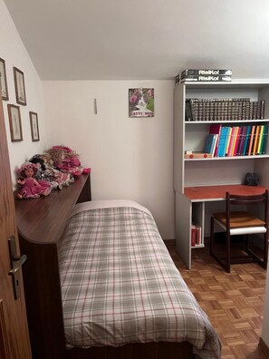 Ein Schlafzimmer mit einem Bett, einem Schreibtisch, einem Stuhl, einem Bücherregal und einer Wand mit gerahmten Bildern.
