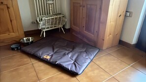 A room with a pet bed, a radiator, a wooden door, and a tiled floor. - 'Il Rifugio del Brunone' Apartment with Mountain View, Balcony and Wi-Fi (Valda)
