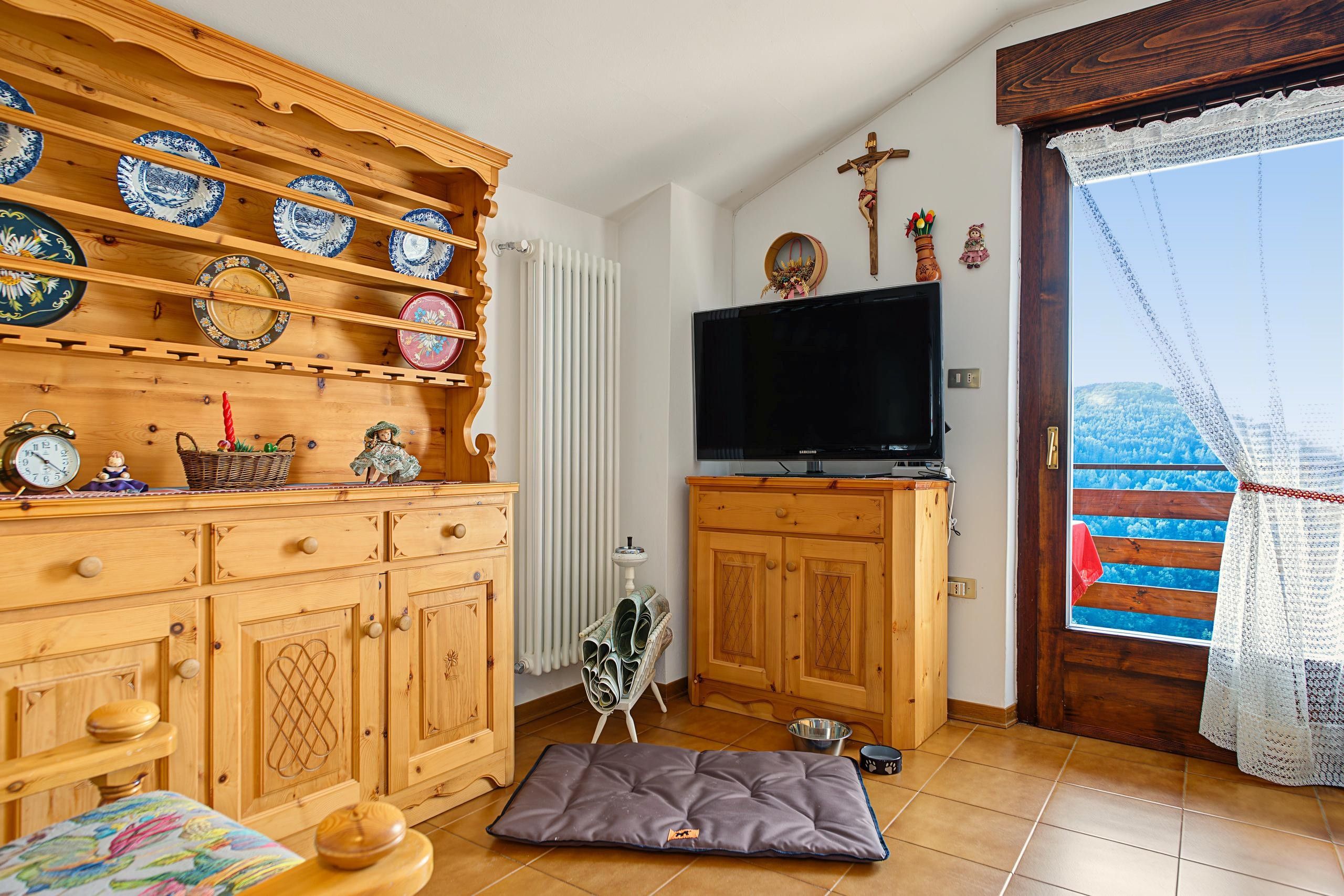 Ein gemütliches Wohnzimmer mit Holzsärchen, einem Flachbildfernseher und einem Fenster mit Blick auf den Himmel.