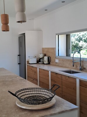 A modern kitchen with a built-in refrigerator, a coffee maker, a kettle, and a sink. - In Provence (Richerenches)