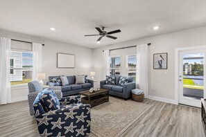 A modern living room with a blue sofa set, a coffee table, and a ceiling fan. - Beach and Pool Games+PaddleBoard+Bikes (Port St. Joe)