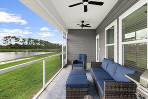 A covered outdoor seating area with a view of a lake, a ceiling fan, and a grill. - Beach and Pool Games+PaddleBoard+Bikes (Port St. Joe)