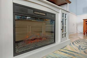 Een moderne open haard met glazen voorpaneel, houten bovenplaat en een vloerkleed met patroon.