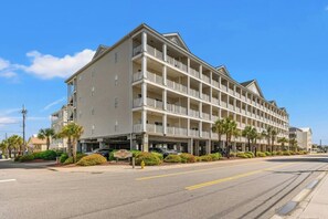 A multi-story hotel with balconies, a parking lot, and a clear sky. - Cherry Grove Villas 410-5BR-Beach Across Street (North Myrtle Beach)