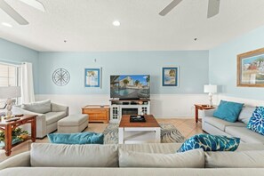 A living room with a sofa, coffee table, and TV stand. - Cherry Grove Villas 410-5BR-Beach Across Street (North Myrtle Beach)