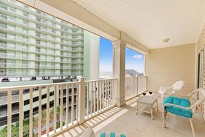 A balcony with a view of a multi-story building, a white chair, a small table, and a blue cushion. - Cherry Grove Villas 410-5BR-Beach Across Street (North Myrtle Beach)
