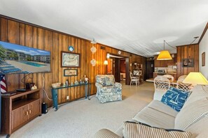 A room with a wooden wall, a sofa, a dining table, and a kitchen area. - Sea Cabin 211- 2 Bedroom with Side Ocean View (North Myrtle Beach)