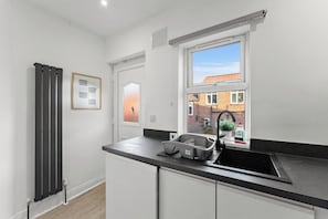 Eine moderne Küche mit schwarzem Arbeitsplatz, einem Fenster mit Blick auf ein Backsteingebäude und einem Heizkörper an der Wand.