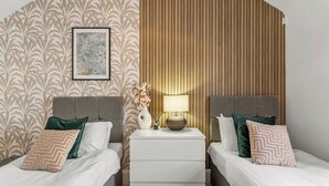 Et hotelværelse med to senge, et natbord med lampe og en dekorativ vægpanel.