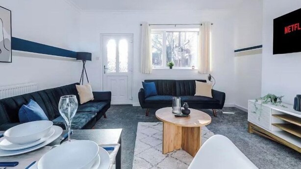 Een moderne woonkamer met een zithoek, een salontafel en een aan de muur bevestigde televisie.