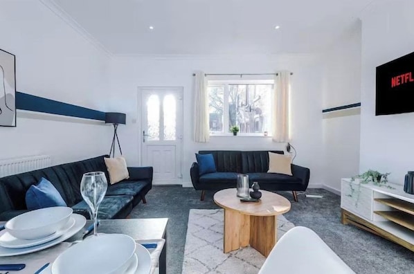 Ein modernes Wohnzimmer mit einer Sofagarnitur, einem Couchtisch und einem an der Wand montierten Fernseher.