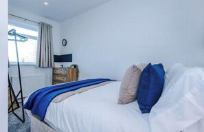 A bedroom with a bed, a dresser, a window with curtains, a radiator, and a clock on the wall. - Elegant 2BR Getaway Near Wakefield | Parking (Wakefield)