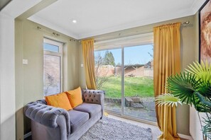 Quarto com sofá cinzento, cortinas amarelas e uma grande janela com vista para uma área gramada.