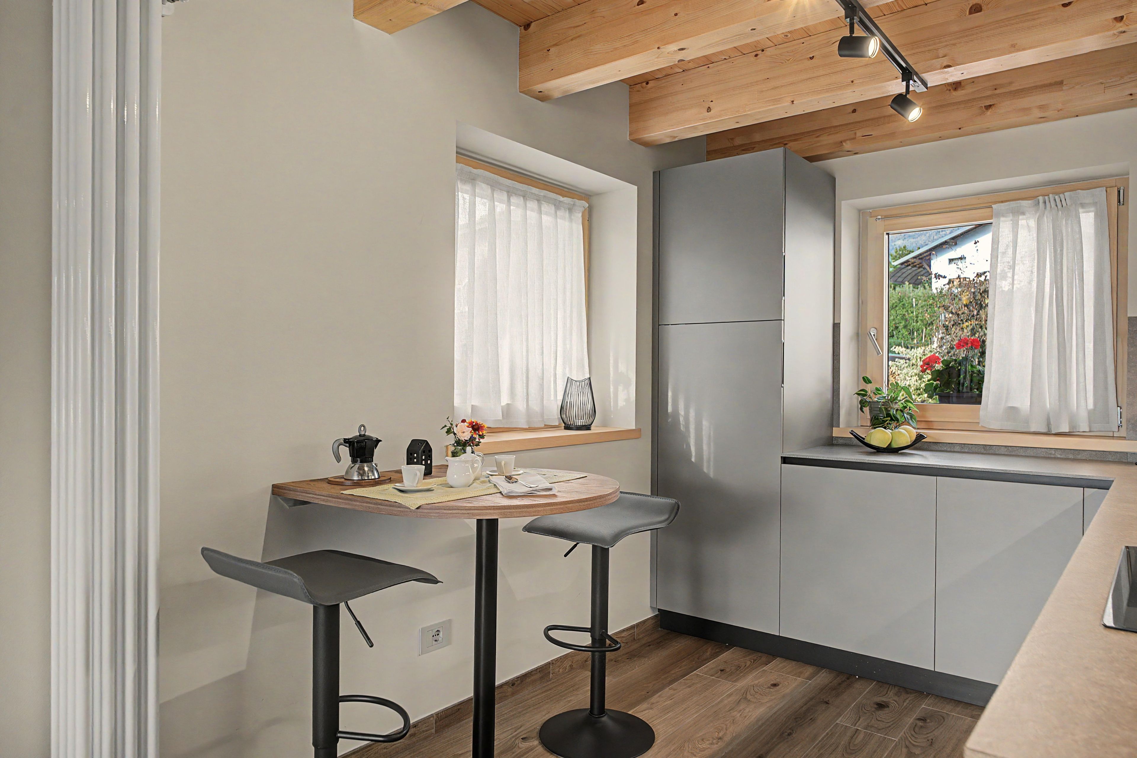 Eine kompakte Küche mit einem runden Tisch, zwei Barhocker, einem Kühlschrank und einem Fenster mit Vorhängen.
