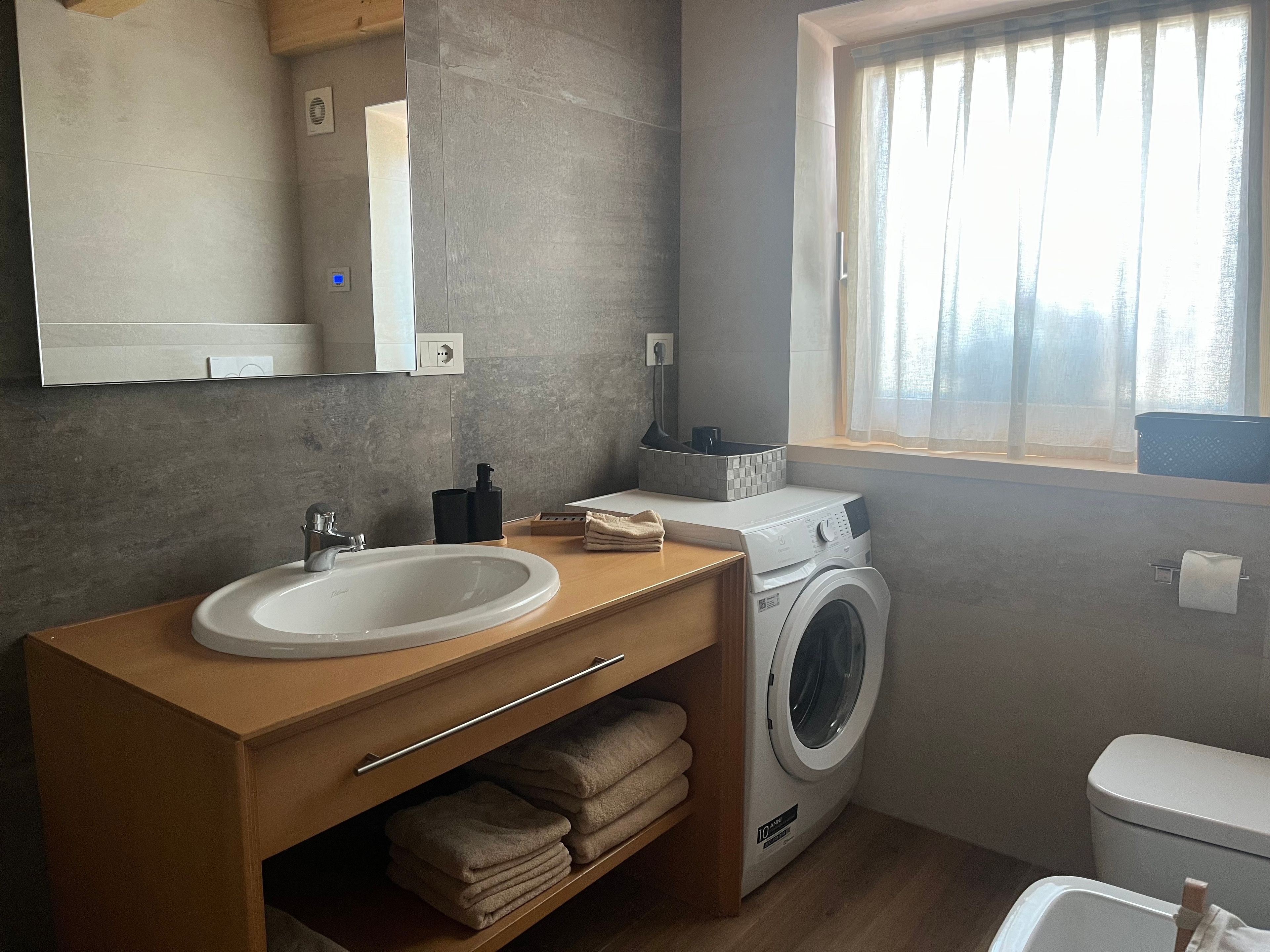 Un bagno moderno con lavandino, specchio, lavatrice e finestra con tende.