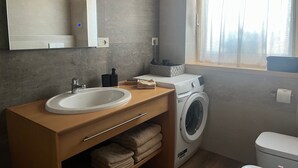 Casa de banho moderna com lavatório, espelho, máquina de lavar roupa e janela com cortinas.