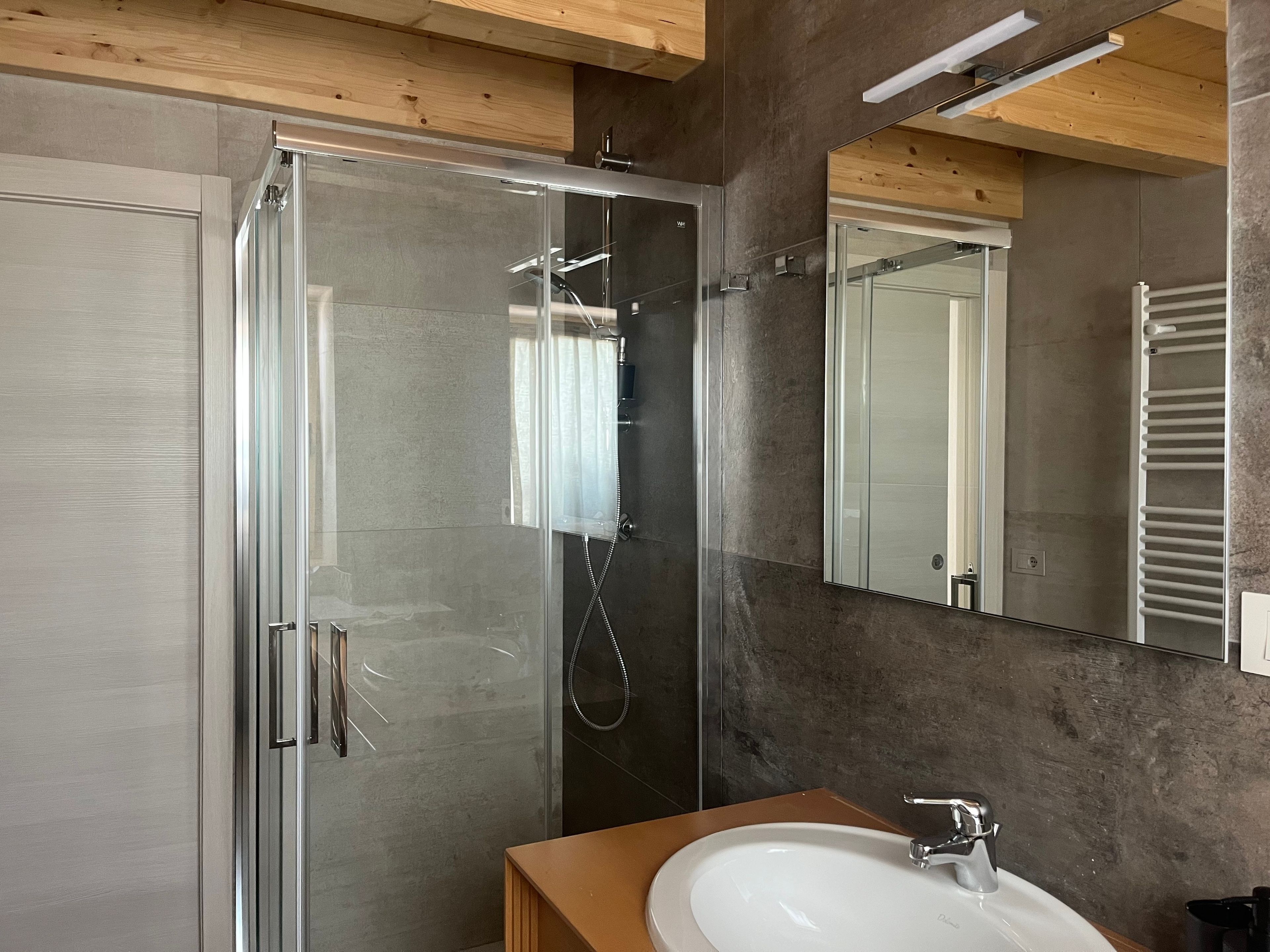 Un bagno moderno con cabina doccia in vetro, lavandino bianco e specchio grande.