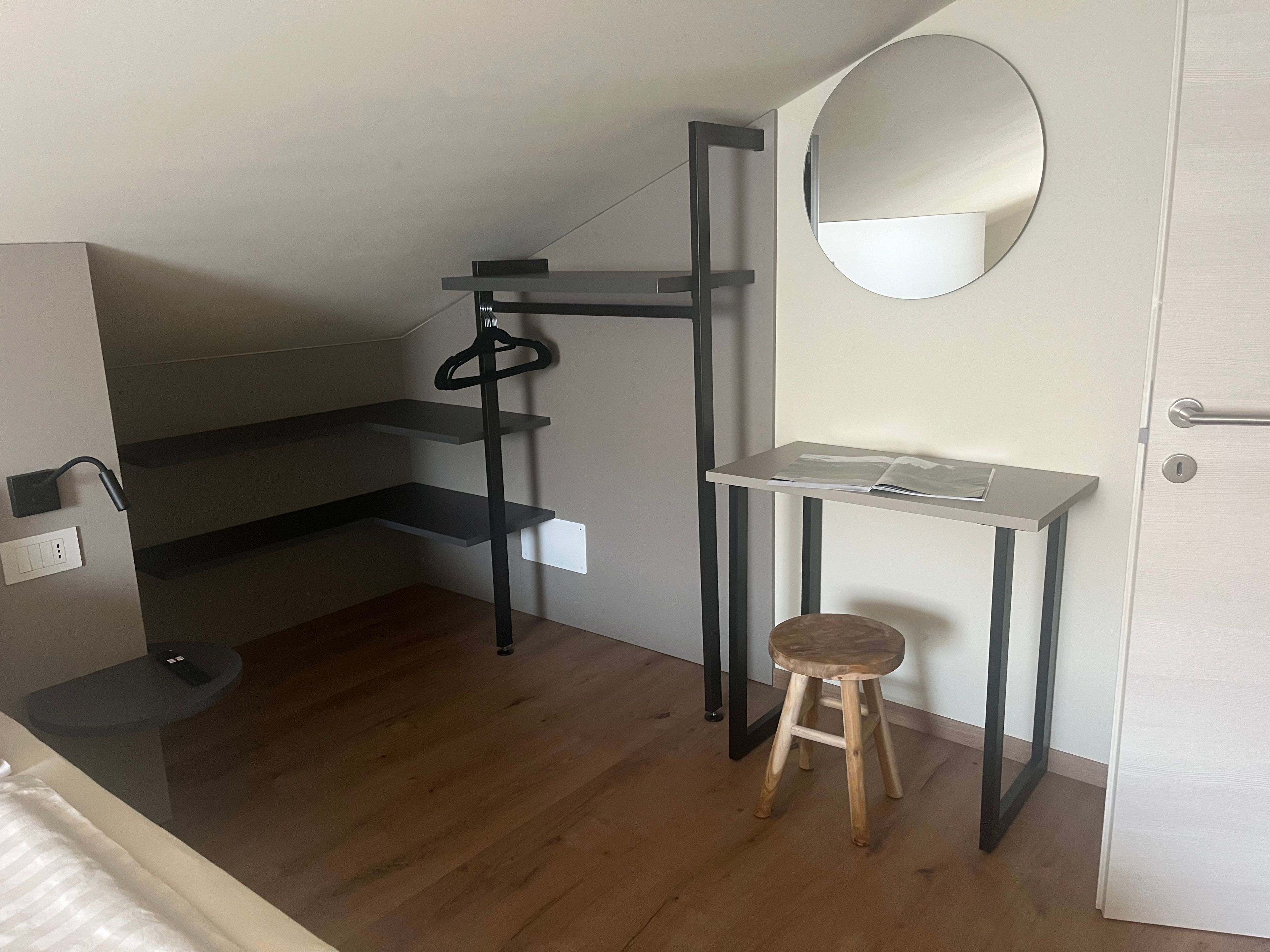 Ein kleiner Raum mit Holzboden, einem kleinen Hocker, einem Schreibtisch mit Spiegel und einer Tür.