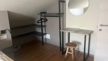 Ein kleiner Raum mit Holzboden, einem kleinen Hocker, einem Schreibtisch mit Spiegel und einer Tür.