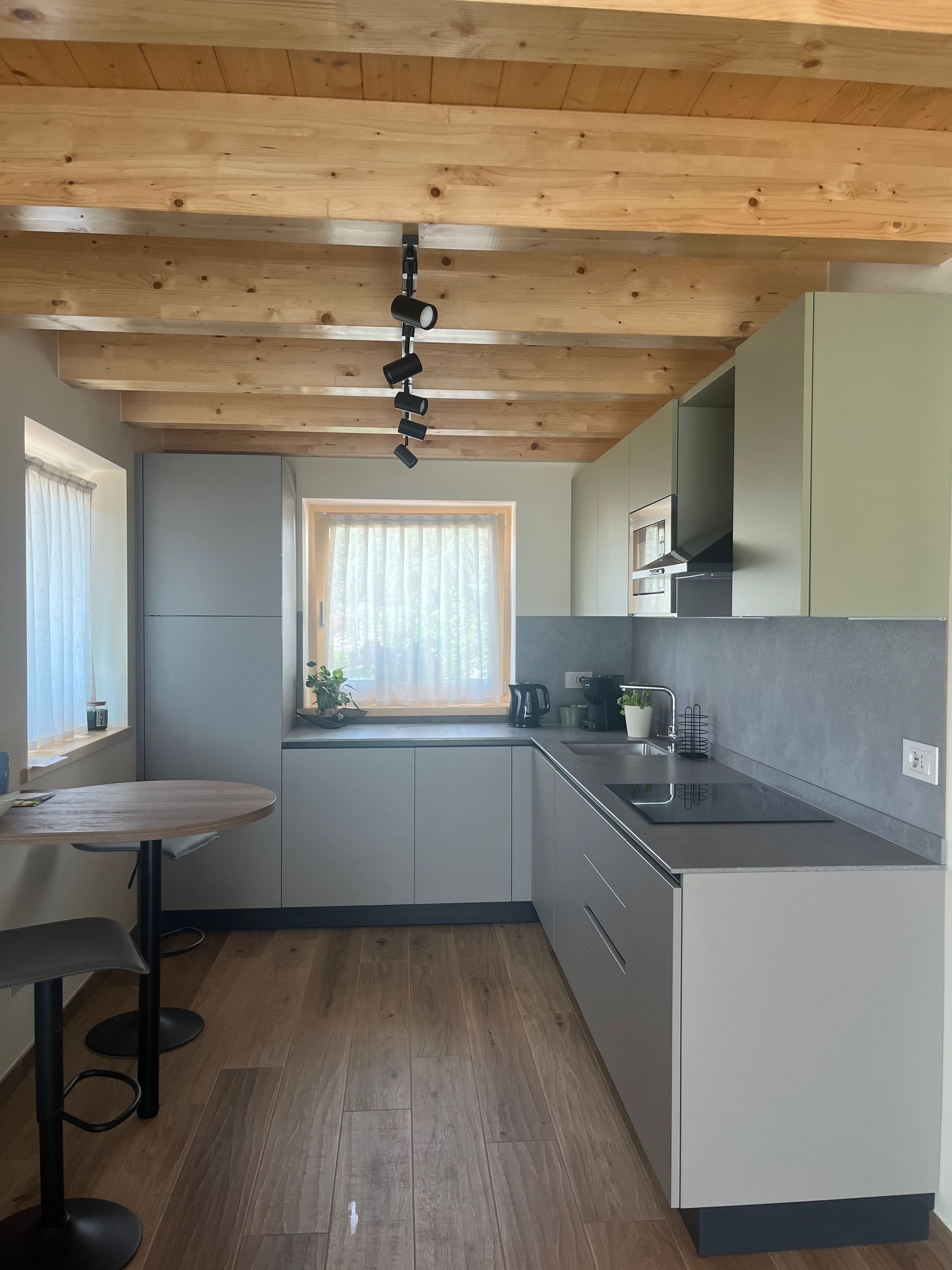 Eine moderne Küche mit Holzbalkendecke, einem fenster mit Vorhängen, einer Spüle und einem kleinen Esstisch mit Stühlen.