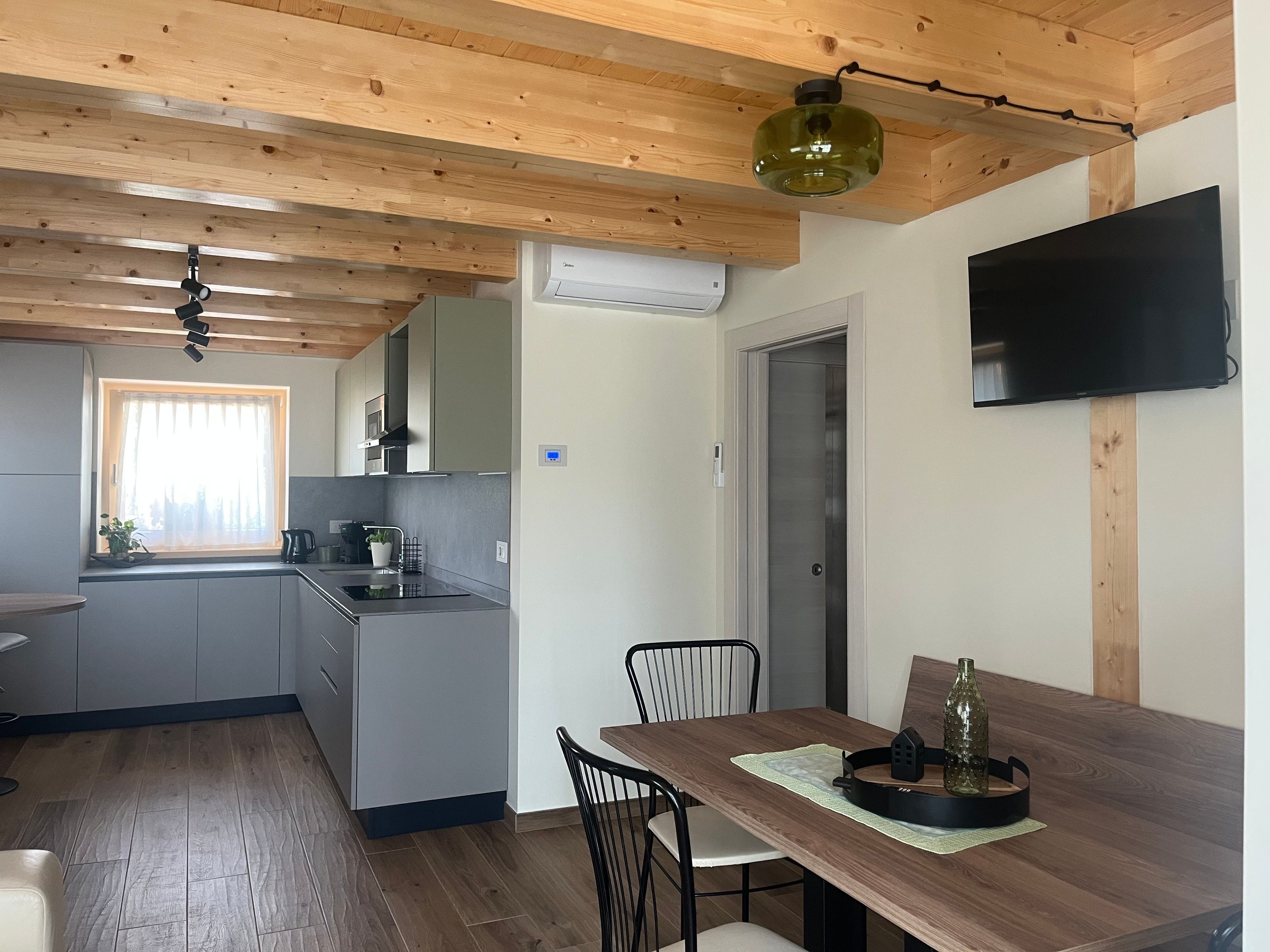 Een moderne keuken met houten balken, een eethoek met tafel en stoelen, en een flatscreen televisie aan de muur.