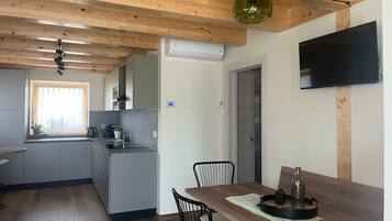 Een moderne keuken met houten balken, een eethoek met tafel en stoelen, en een flatscreen televisie aan de muur.