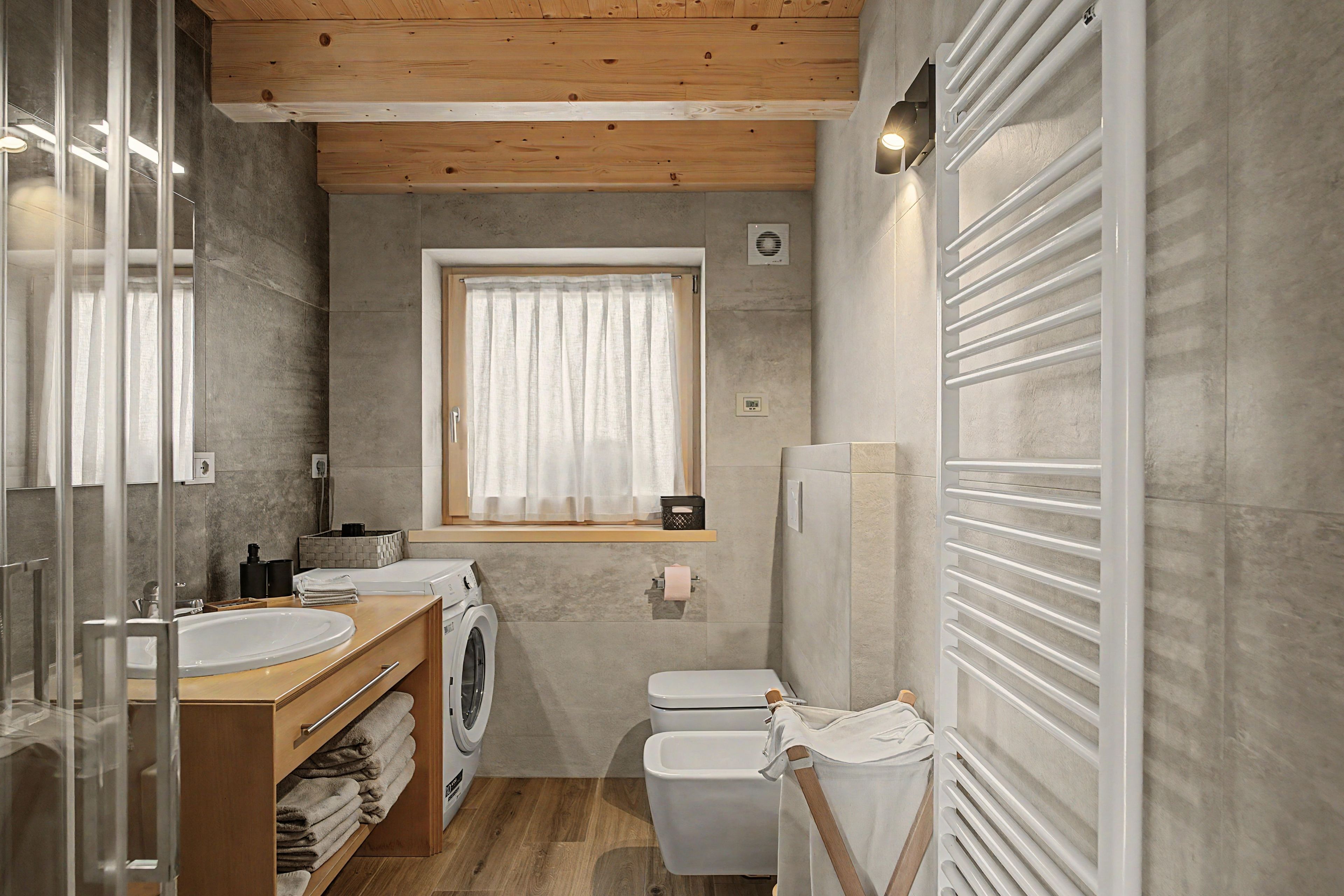 Un baño moderno con techo de madera, un espejo grande, un lavamanos, una lavadora y un inodoro.