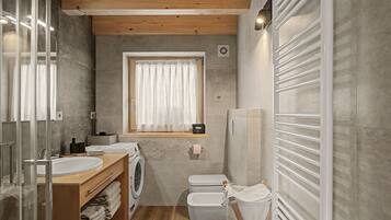 Un baño moderno con techo de madera, un espejo grande, un lavamanos, una lavadora y un inodoro.