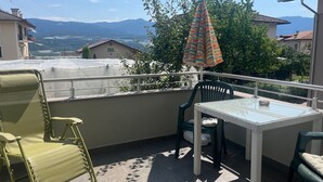 Uma varanda com mesa e cadeiras, um guarda-sol estampado e vista para montanhas ao longe.