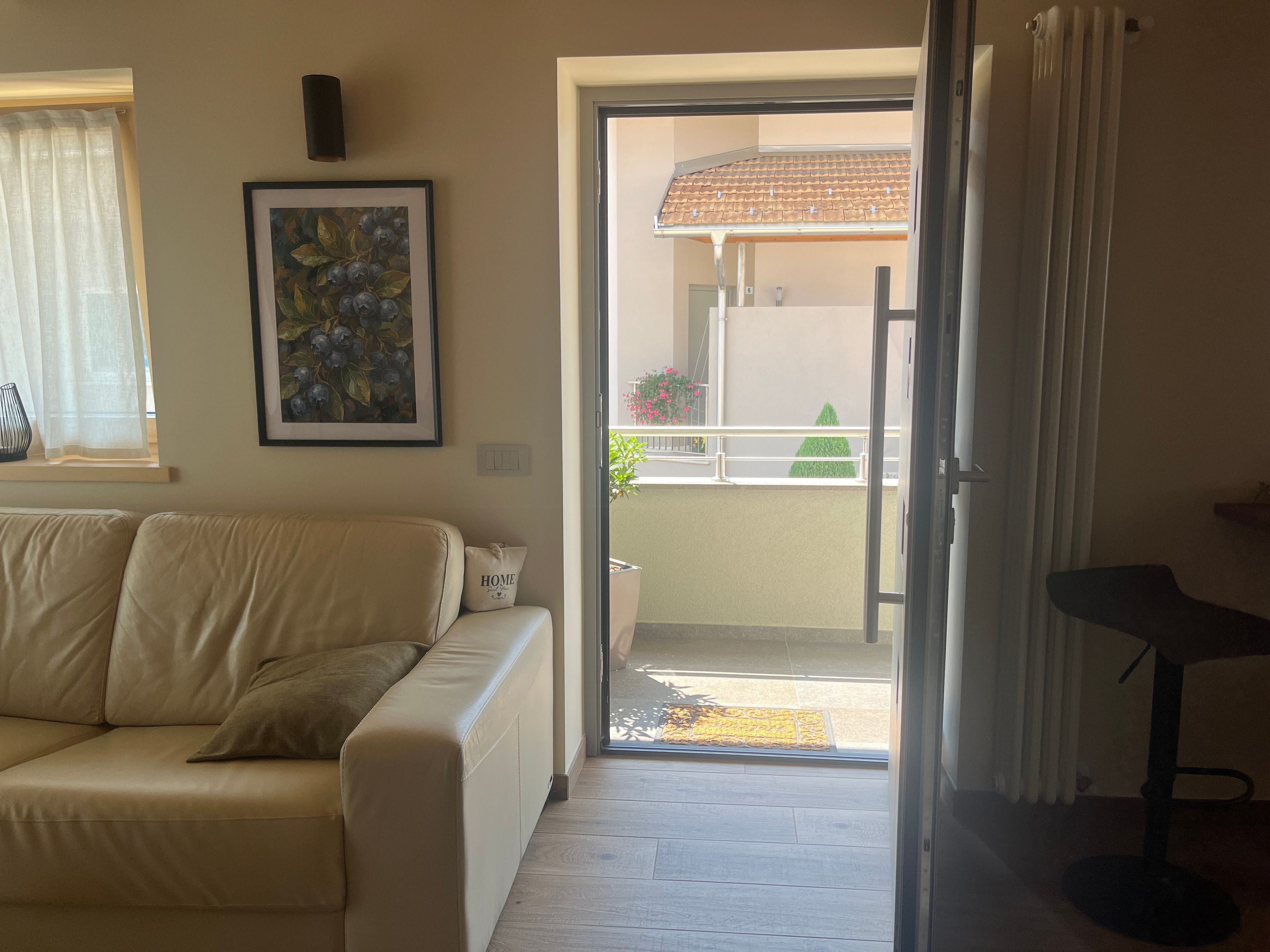 Een woonkamer met een bank, een ingelijst kunstwerk, een bijzettafeltje en een schuifdeur naar een buitenruimte met een betegeld dak en planten.