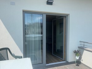 Puerta corrediza de vidrio que da a un espacio interior con una silla y una pequeña planta en maceta.