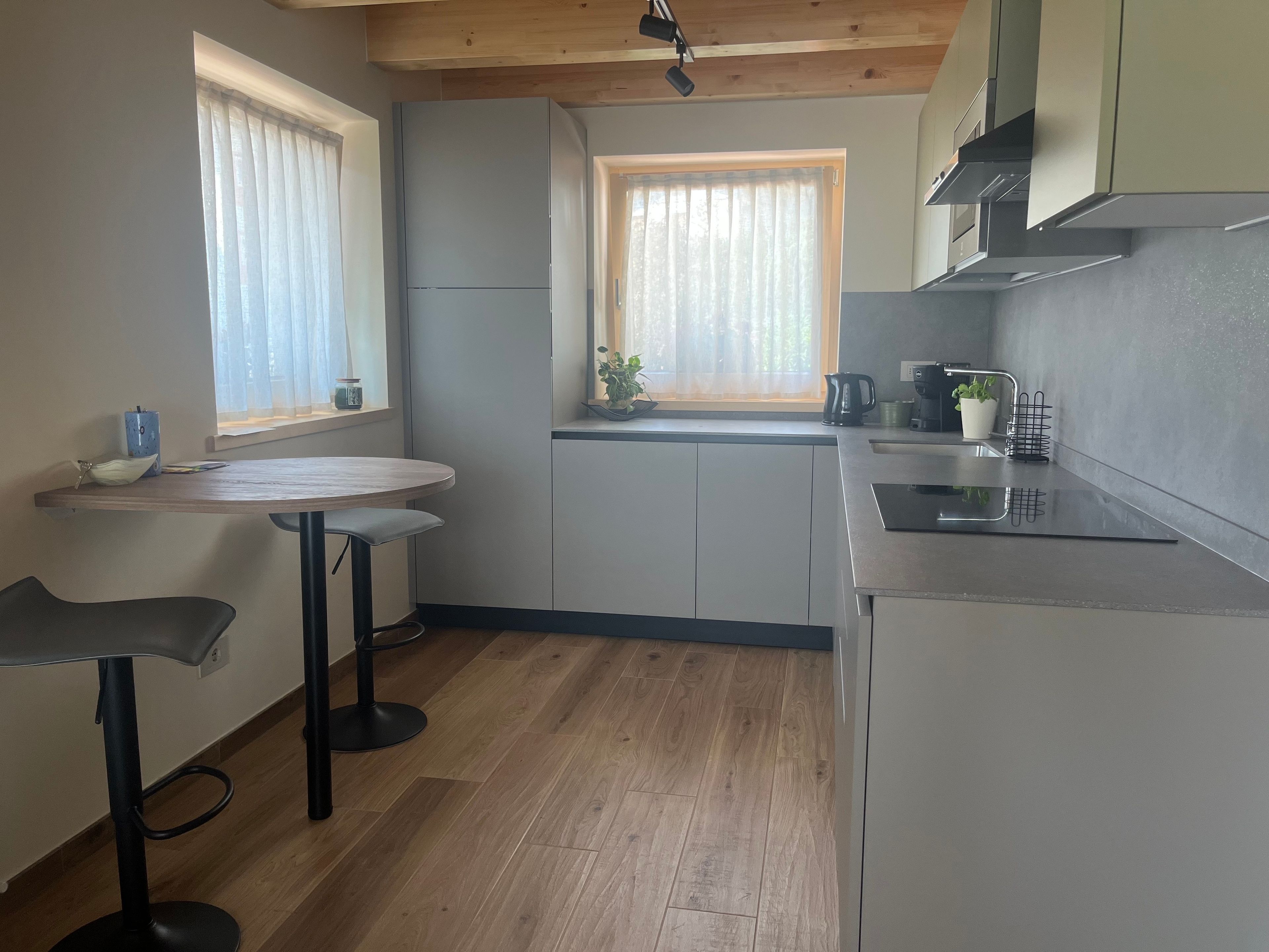 Een moderne keuken met een houten plafond, een eethoek met een ronde tafel en twee stoelen, en een raam met uitzicht op groen.