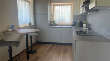 Een moderne keuken met een houten plafond, een eethoek met een ronde tafel en twee stoelen, en een raam met uitzicht op groen.