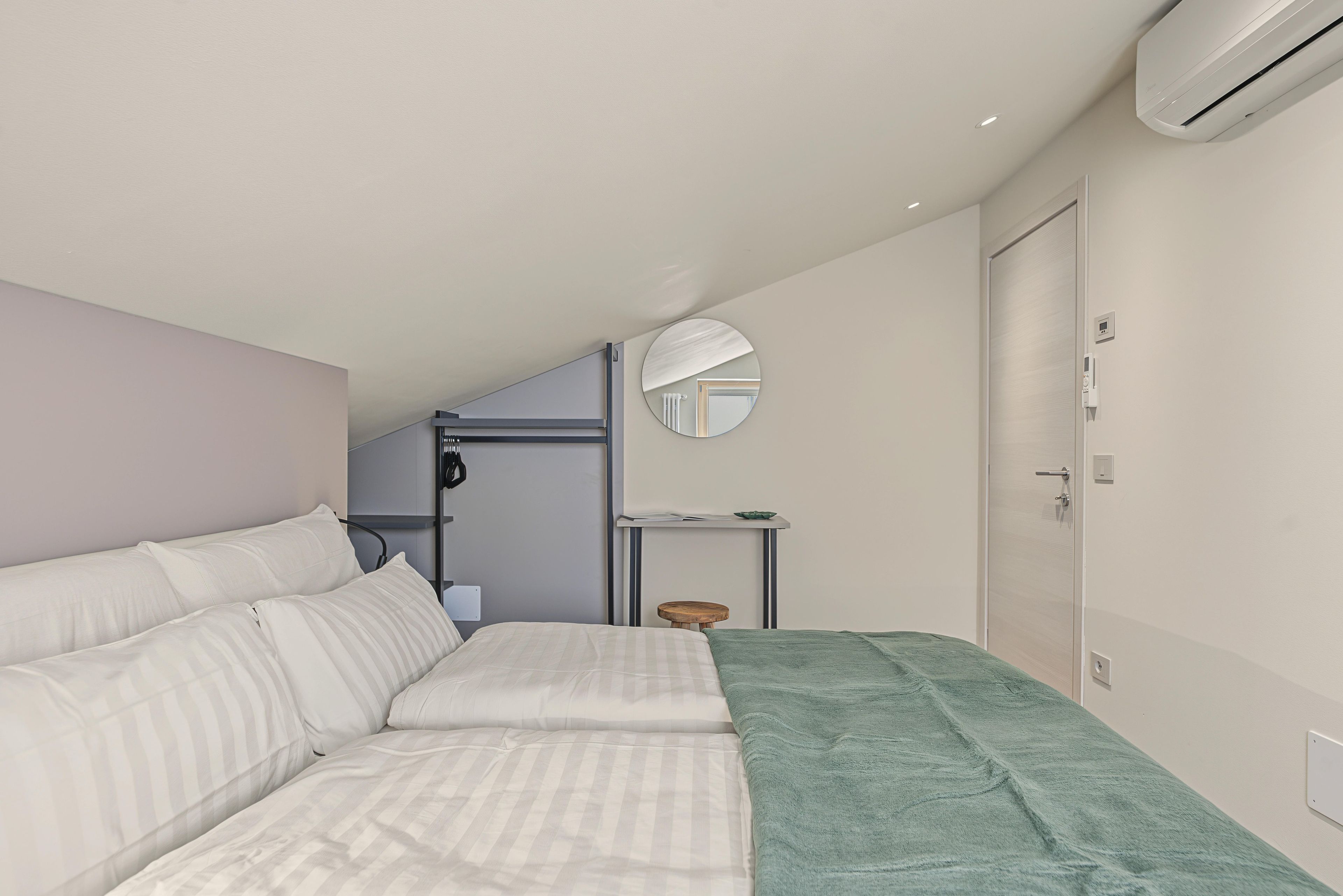 A modern bedroom with a bed, a bedside table, a mirror, and an air conditioning unit.
