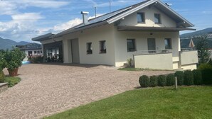 Uma casa de dois andares com telhado inclinado, varanda coberta e entrada pavimentada.