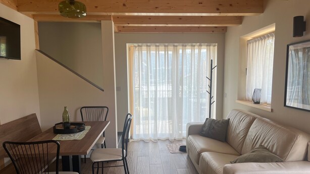 Uma sala de estar moderna com uma mesa de jantar de madeira, cadeiras, um sofá e uma escada.