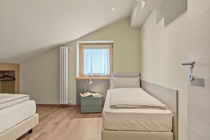 A small, single-bedroom room with a sloped ceiling, a window with a curtain, a bedside table with a lamp, and a radiator.