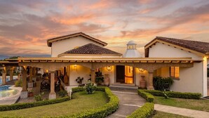 Una casa de dos pisos con un porche cubierto, una piscina y un jardín bien cuidado.