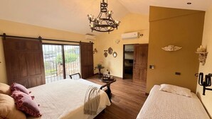 Un dormitorio con una cama grande, una cama más pequeña, una araña de cristal y vistas a través de un ventanal corredero.