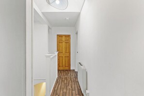 Ein schmaler Flur mit weißen Wänden, einer Holztür am Ende und einem Heizkörper an der rechten Seite.