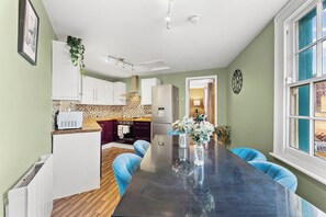 Une cuisine moderne avec des meubles blancs, un plan de travail noir et un coin repas comprenant une table noire et des chaises bleues.