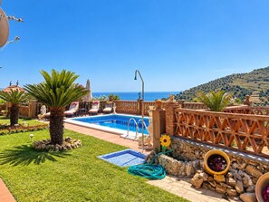 Ein Swimmingpool mit Meerblick, umgeben von einem Garten mit Palmen und einer Steinmauer.